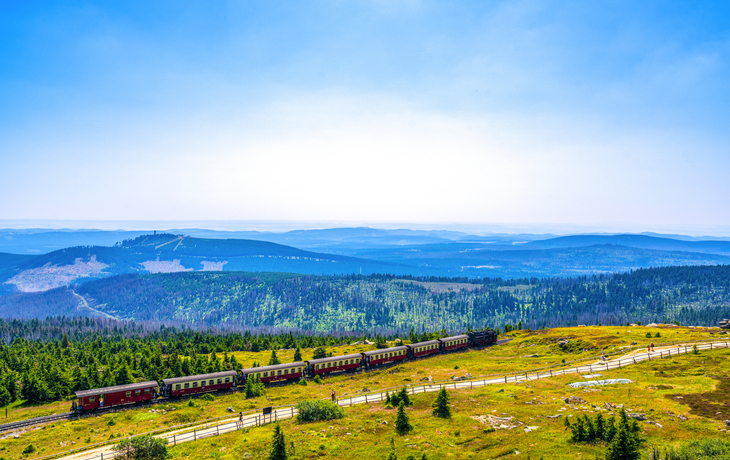 Zug fährt durch bergige Waldlandschaft unter klarem Himmel.