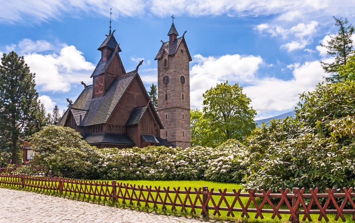 Holzkirche mit Turm, umgeben von Bäumen und einem Holzzaun.