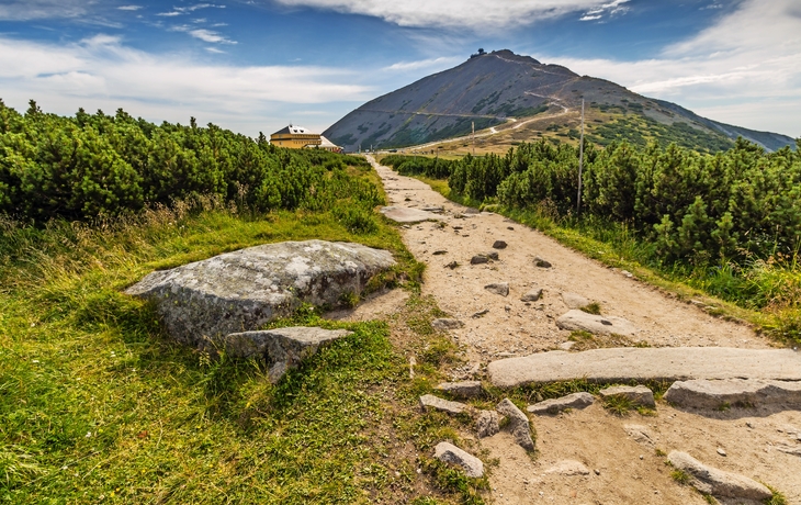 Wanderweg in einer Berglandschaft mit blauem Himmel und Wolken.