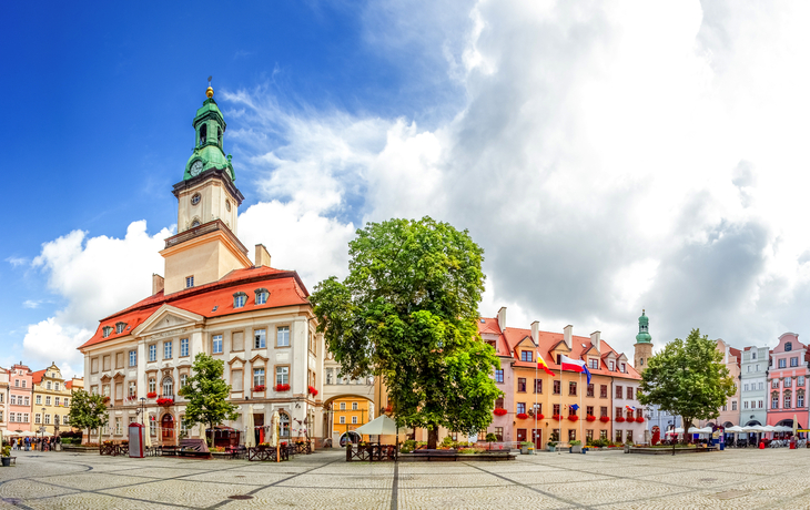Historischer Platz mit bunten Gebäuden und einem Turm unter blauem Himmel.
