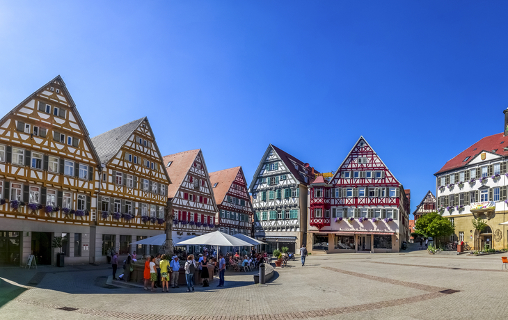 Marktplatz mit historischen Fachwerkhäusern und Menschen an einem sonnigen Tag.