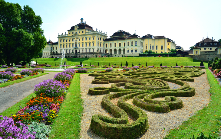 Barockschloss mit gepflegtem Garten und blühenden Blumenrabatten im Vordergrund.