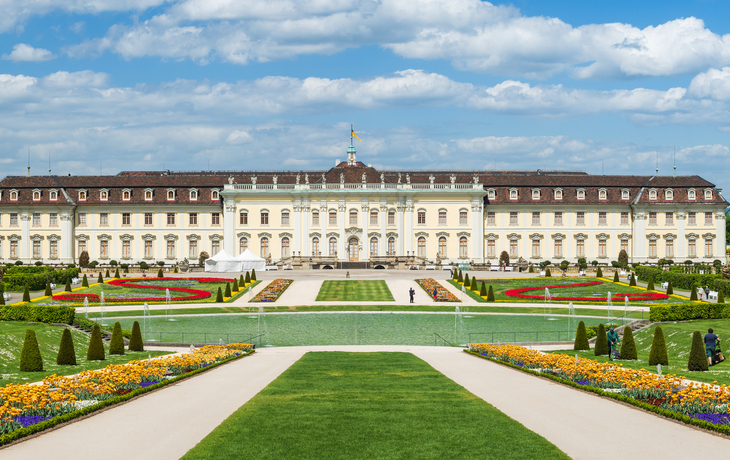 Blick auf ein großes Barockschloss mit gepflegtem Garten im Vordergrund.