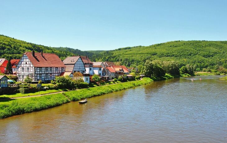 Fachwerkhäuser am Fluss in Gieselwerder, umgeben von grünen Hügeln.