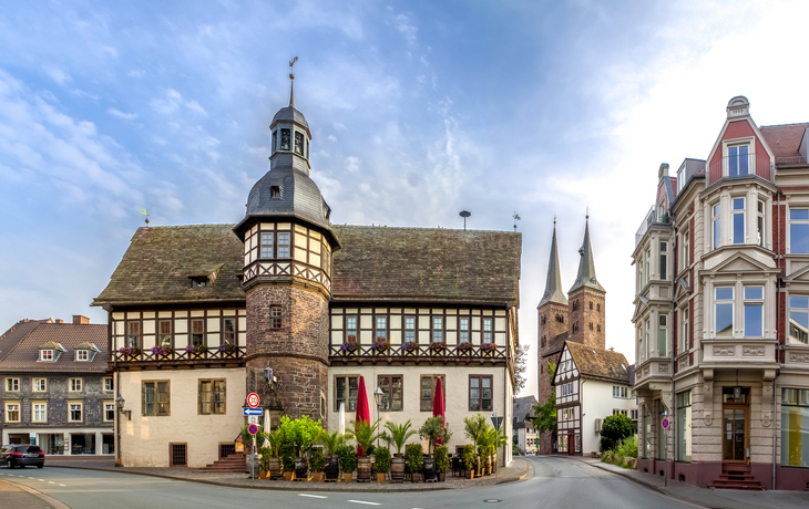 Fachwerkgebäude an Straßenecke mit Kirchtürmen im Hintergrund.