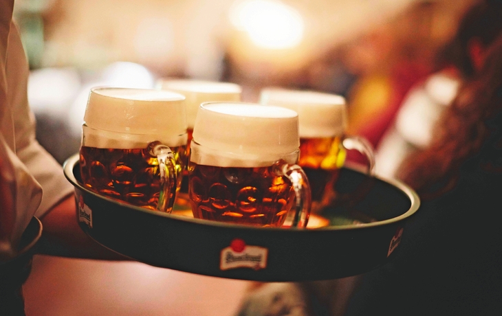 Ein Tablett mit vier Gläsern Bier, die von einer Person getragen werden.