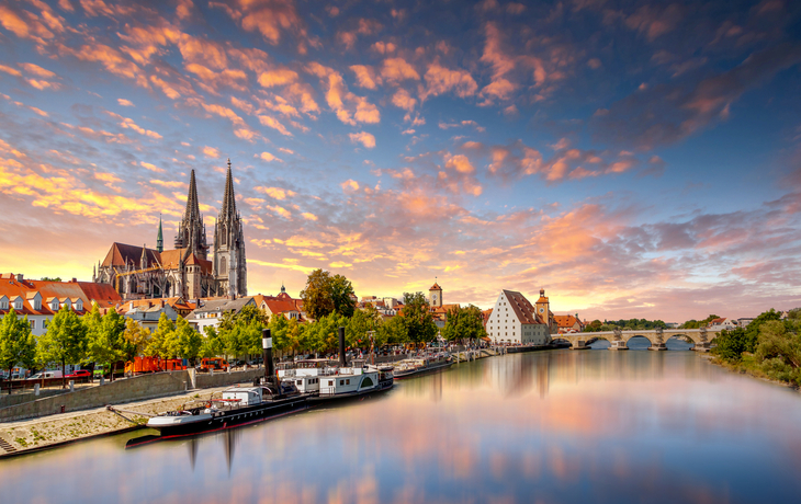 Städtische Flusslandschaft mit Kirche und Brücke im Sonnenuntergang.