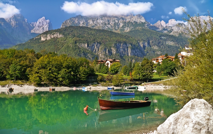 Holzboote auf einem klaren Bergsee mit bewaldeten Ufern und Bergkulisse.