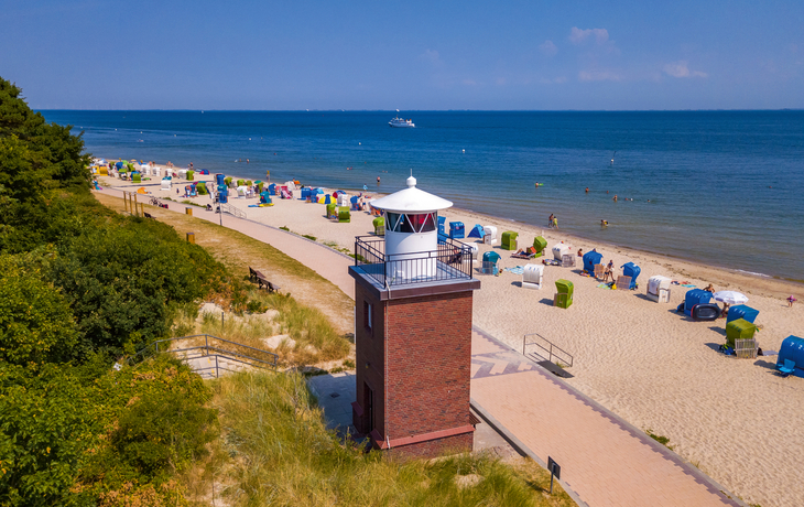 Leuchtturm am Sandstrand mit Strandkörben und Meer im Hintergrund.