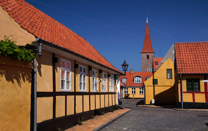 Malerische Altstadtgasse mit Fachwerkhäusern und Kirchturm im Hintergrund.