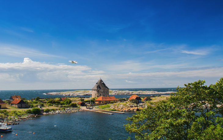 Küstenlandschaft mit historischem Gebäude, blauer Himmel und Meer im Hintergrund.
