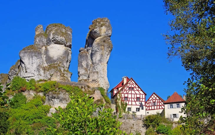 Felsenformation neben traditionellem Fachwerkhaus mit rotem Dach unter klarem, blauem Himmel.