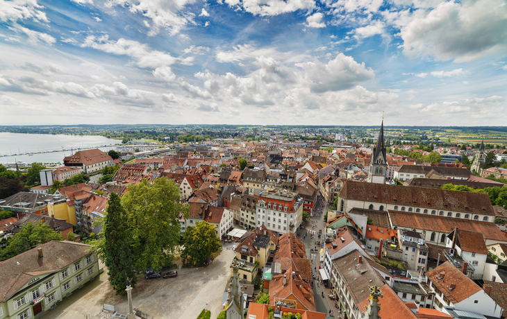 Panoramablick auf eine historische Stadt mit Kirche und See im Hintergrund.