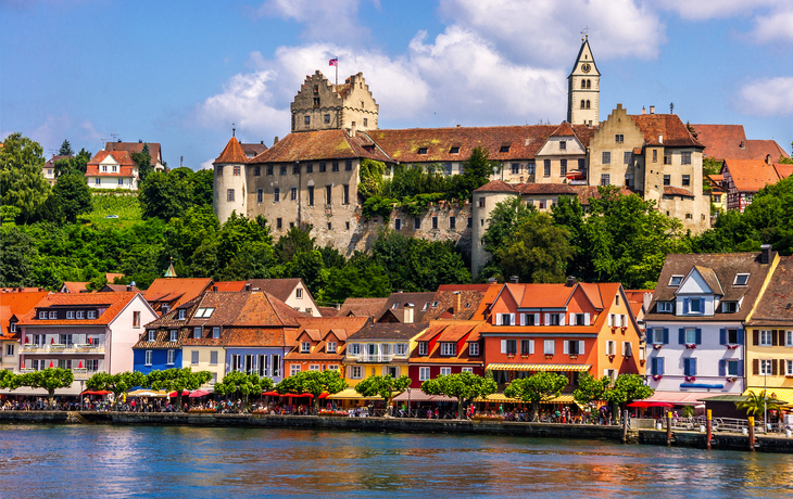 Bunte Häuserfassade und Schloss am Bodensee bei blauem Himmel.