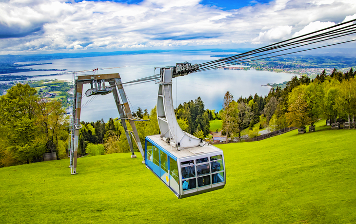 Seilbahn über grüne Wiese mit Blick auf See und Berge im Hintergrund
