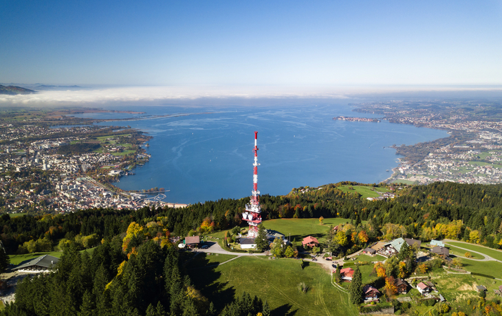 Luftaufnahme eines Sendemastes und Bodensee vor Alpenkulisse.