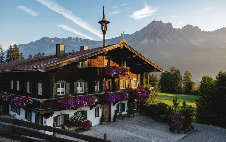 Traditionelles Holzhaus mit Blumen vor Bergkulisse bei Sonnenschein.