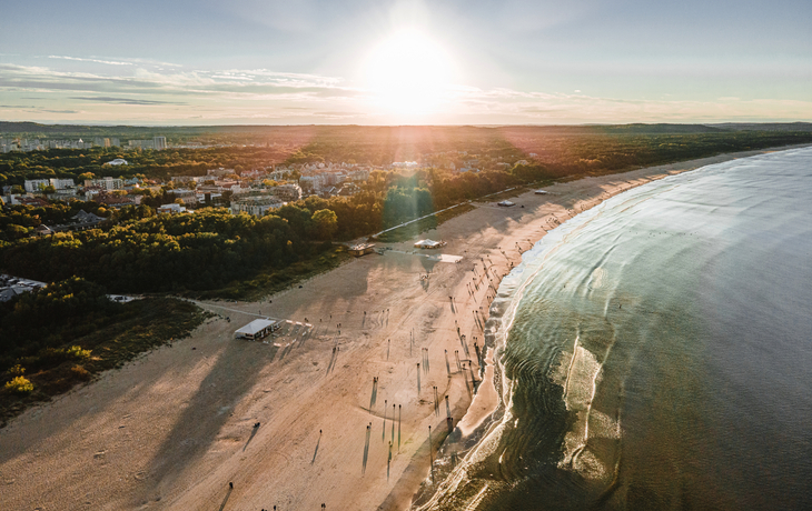 Strandansicht bei Sonnenuntergang mit Bäumen und Stadt im Hintergrund.