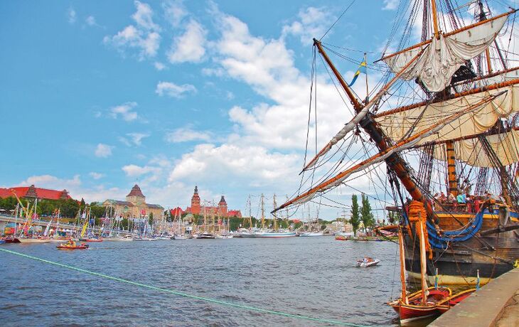 Segelschiff im Hafen vor städtischem Hintergrund bei klarem Himmel.