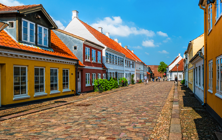 Bunte Häuserzeile entlang einer gepflasterten Straße bei sonnigem Wetter.