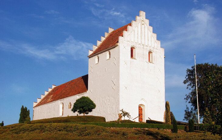 Weiße Kirche mit rotem Dach auf einer Anhöhe unter blauem Himmel.