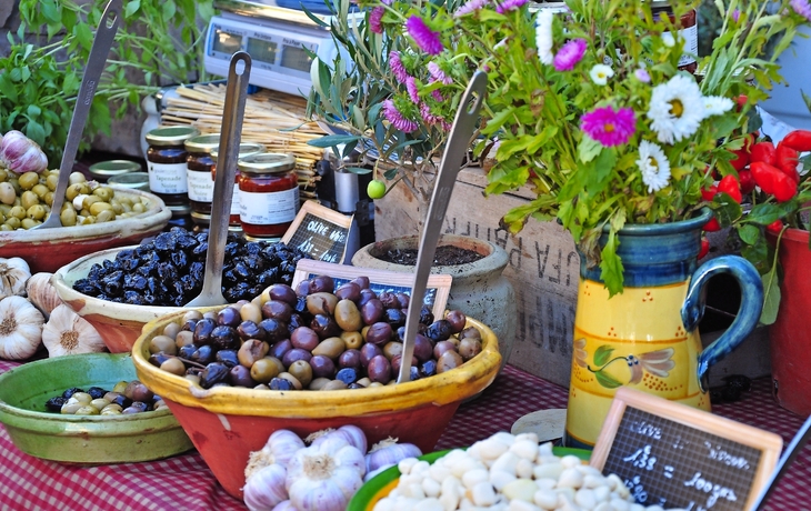 Mischung aus Oliven und Knoblauch auf einem Marktstand mit Blumen und Kräutern.