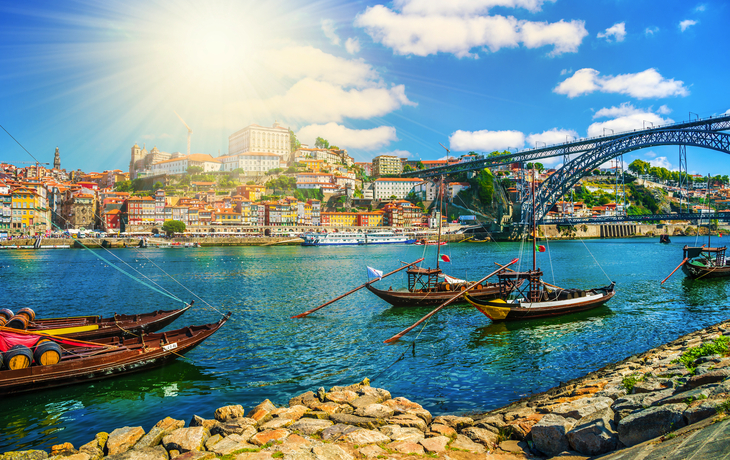 Flussblick mit Booten, Brücke und farbenfroher Stadt bei Sonnenschein.