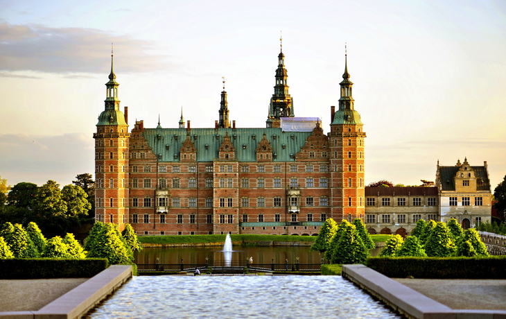 Schloss vor Teich und Bäumen im Sonnenuntergang.