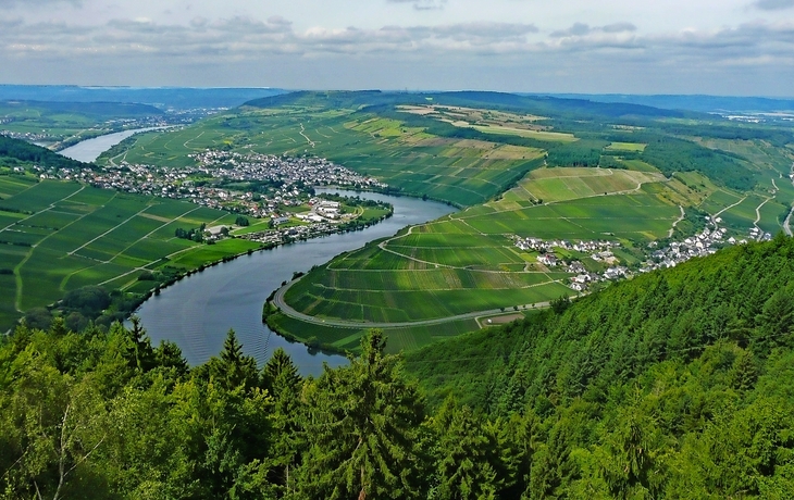 Landschaftsansicht mit Fluss, Hügeln und Wald im Vordergrund.