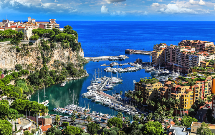 Hafen von Monaco mit Yachten und Gebäuden vor blauem Meer und Himmel.