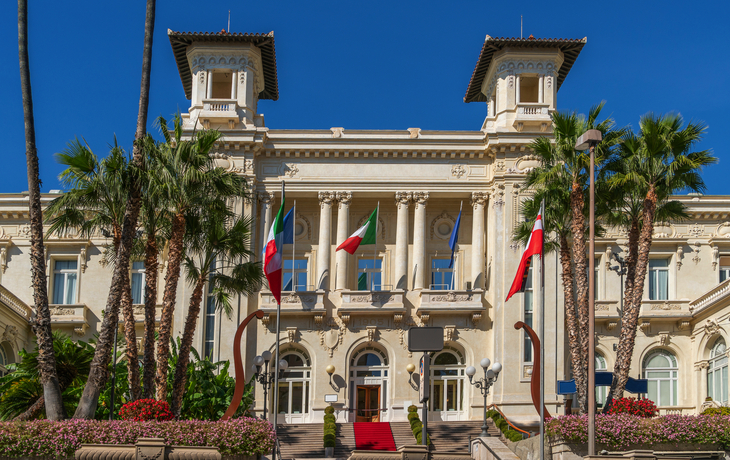 Historisches Gebäude mit Flaggen und Palmen.